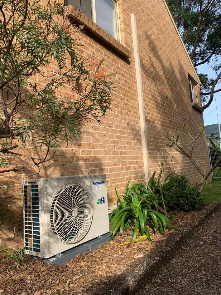Outdoor Air Conditioner Unit Beside a Brick House Wall — Rapidcool Air Conditioning & Electrical In Illawarra, NSW