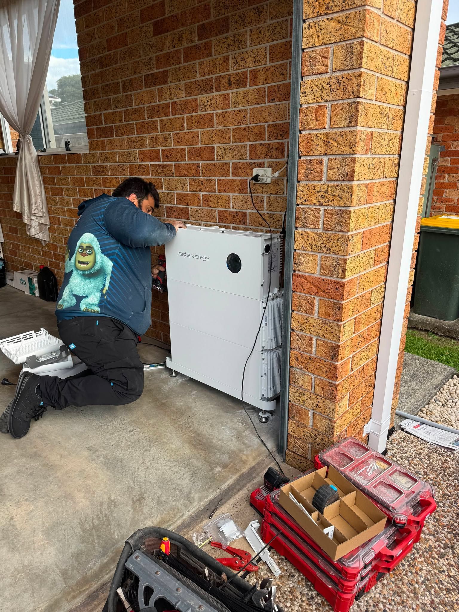 Technician Kneeling by a White Outdoor Electrical Panel — Rapidcool Air Conditioning, Electrical & Solar In Dapto, NSW