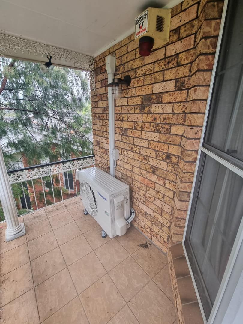 A Mitsubishi Air Conditioner Is Being Repaired On A Brick Sidewalk — Rapidcool Air Conditioning & Electrical In Dapto, NSW