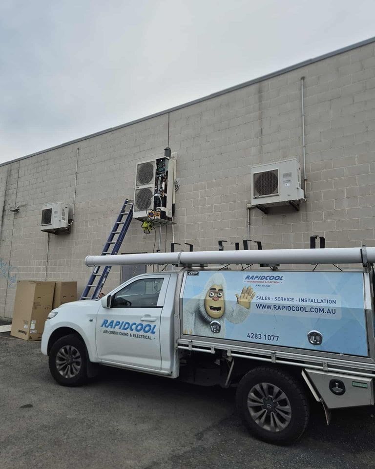 Worker on Ladder Servicing an Air Conditioner — Rapidcool Air Conditioning & Electrical In Wollongong, NSW
