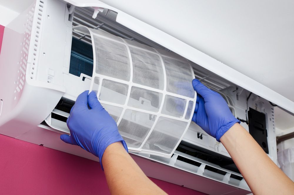A Person Wearing Blue Gloves Is Cleaning An Air Conditioner — Rapidcool Air Conditioning & Electrical In Dapto, NSW