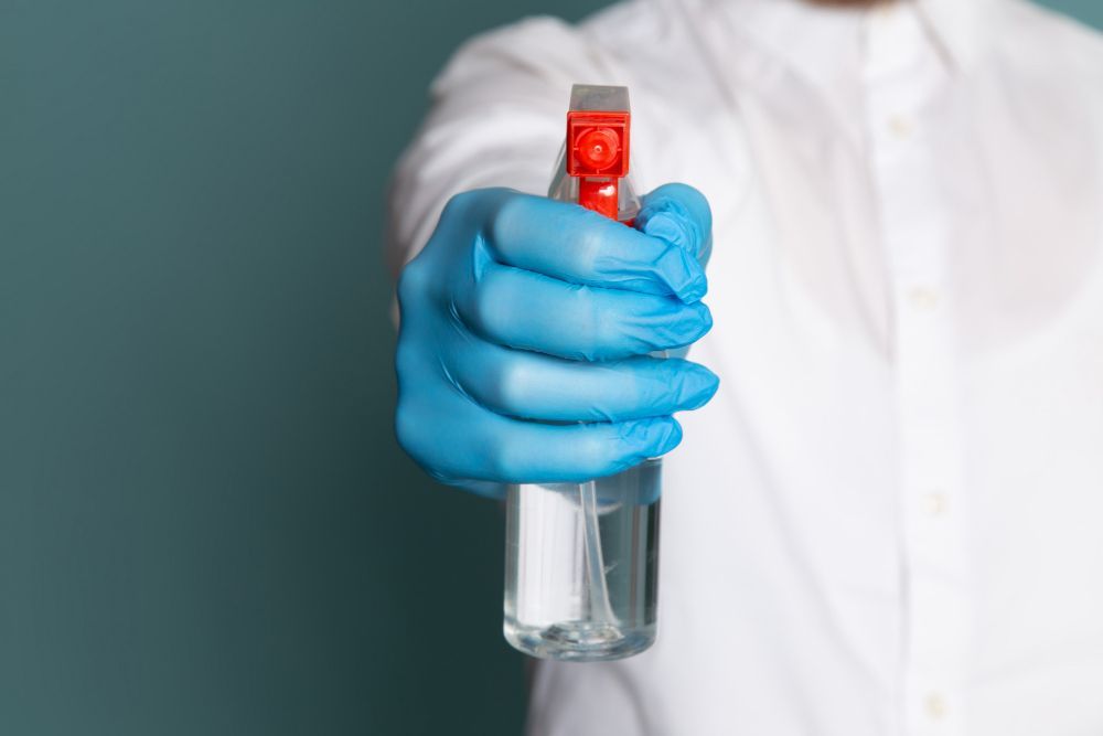 Mano enguantada sosteniendo un pequeño frasco con tapa roja sobre un fondo de bata de laboratorio.