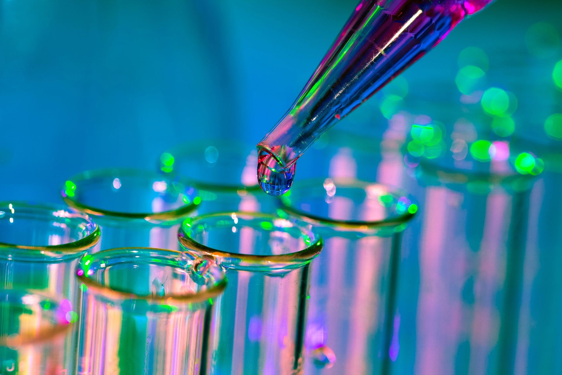Pipeta que dispensa líquido de colores en tubos de ensayo de laboratorio bajo iluminación azul y rosa.