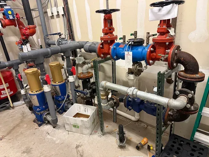 Mechanical room with red and blue piping, valves, and insulated pipes on a concrete floor