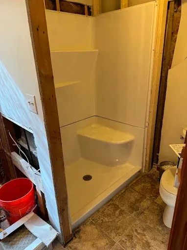 Partially built shower stall with white walls and a raised shower pan in a bathroom under renovation