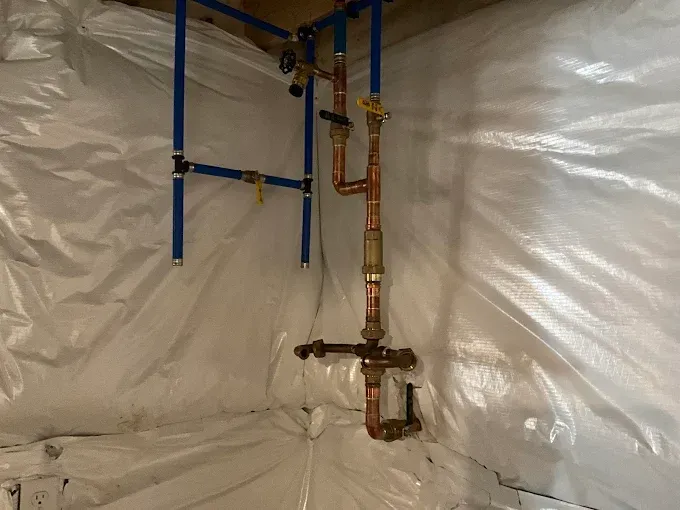Plumbing pipes and shutoff valve inside a plastic-covered crawlspace or utility area