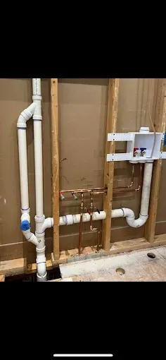 Exposed plumbing with white pipes and copper lines inside an unfinished wall cavity