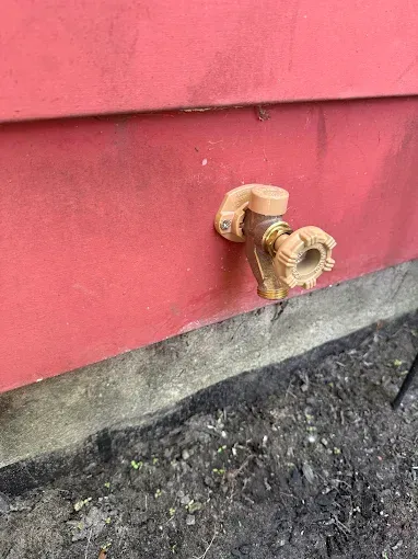Close-up of two rusty outdoor water spigots on a red wall above gravel ground