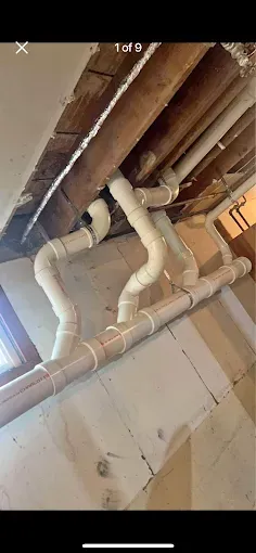 Exposed white pipes and ductwork running across a basement ceiling above cinderblock walls.