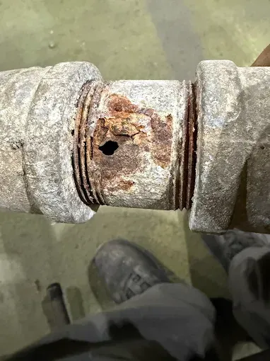 Rusty metal pipe joint with a hole and corroded fittings on a concrete floor