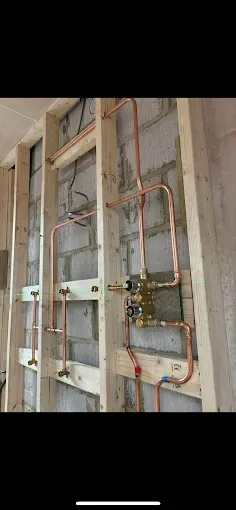 Exposed wall framing with electrical wiring, pipes, and mounted utility boxes during construction