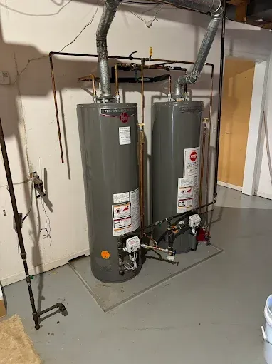 Two water heaters with vent pipes and plumbing in a utility room