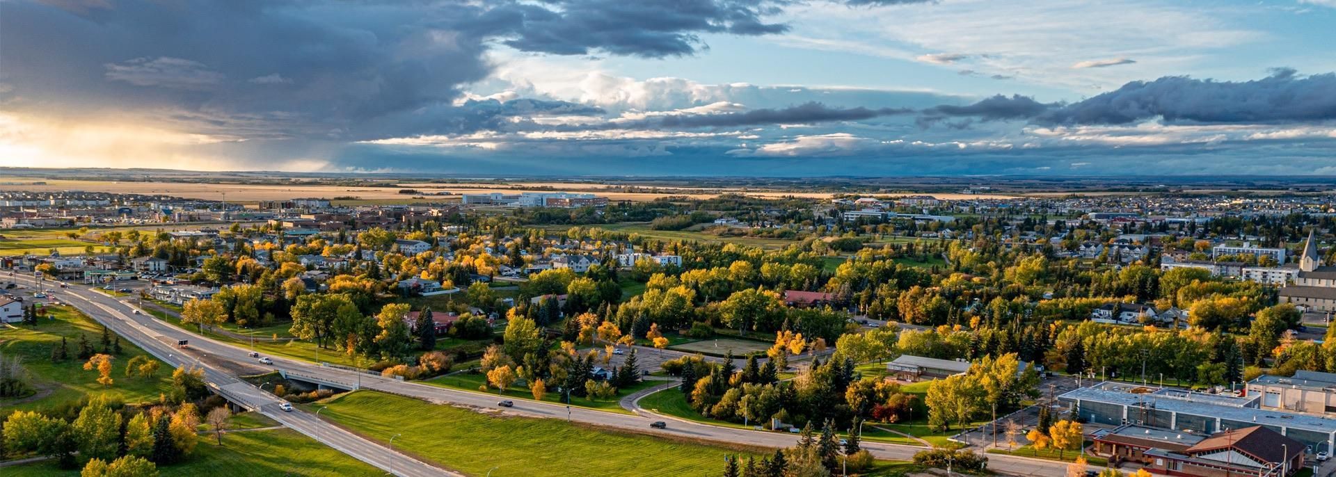 An aerial view of a city surrounded by trees and a road.