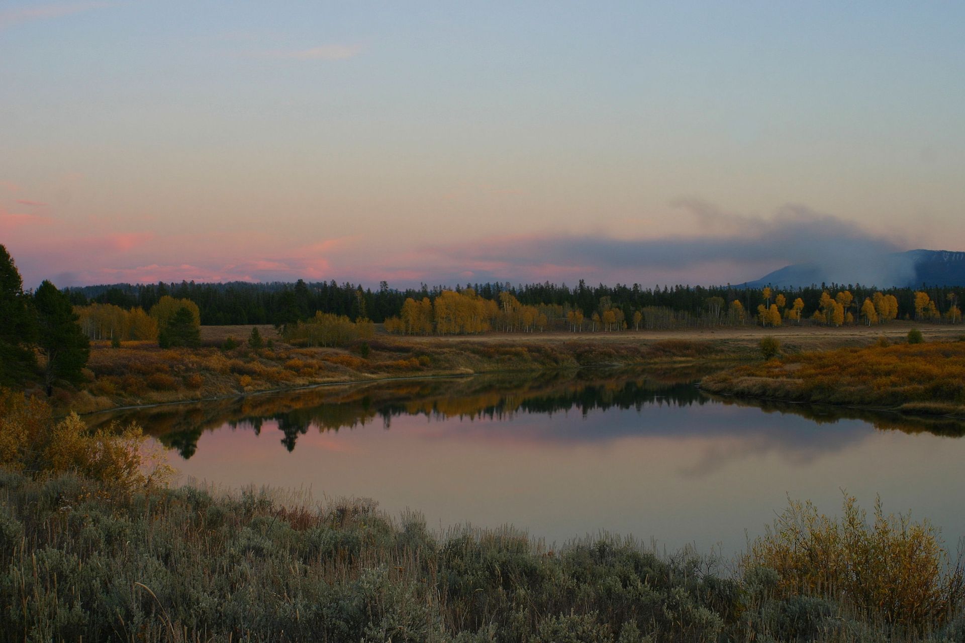 There is a lake in the middle of a field with trees in the background.