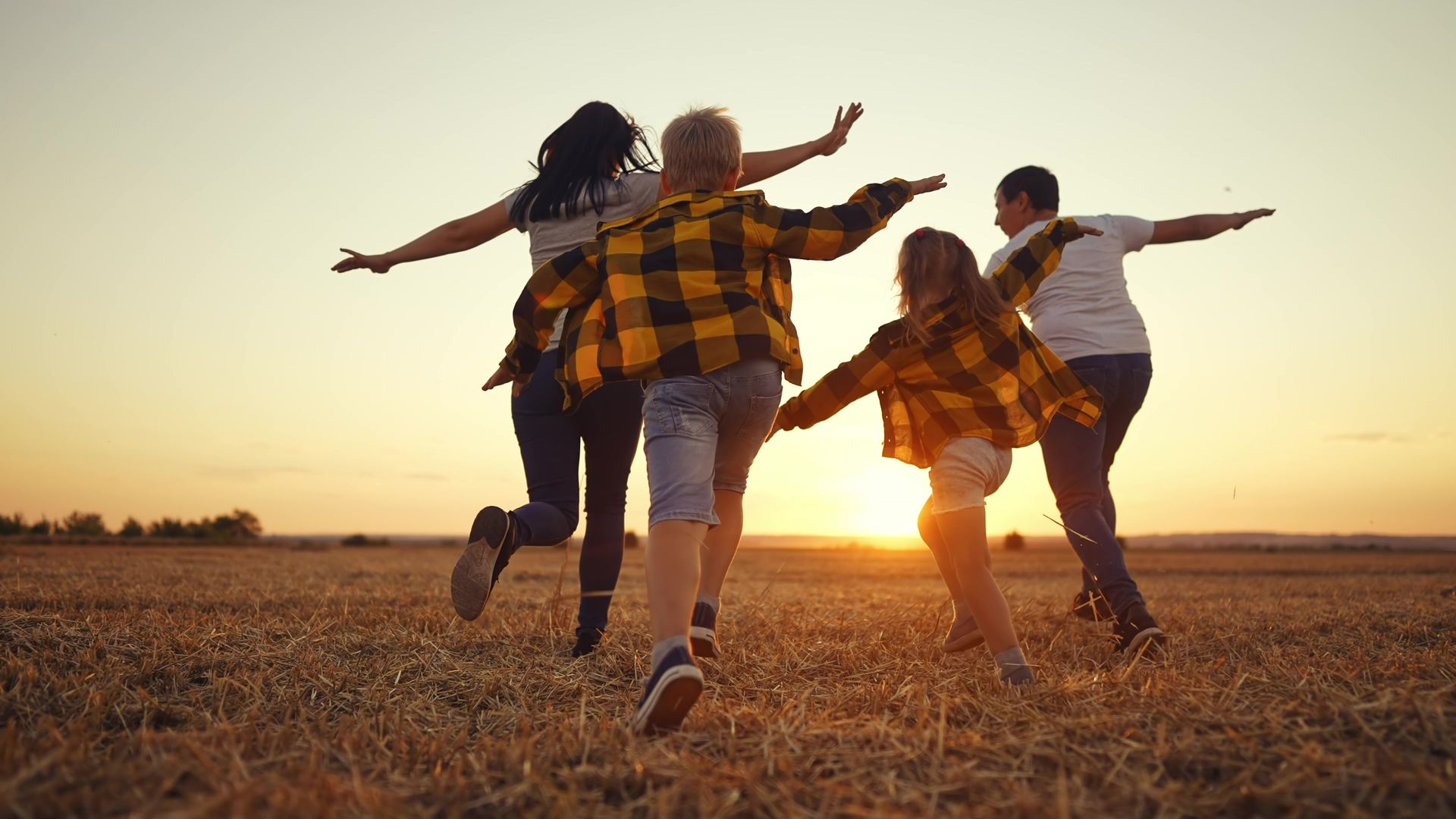 A group of people are running in a field at sunset.