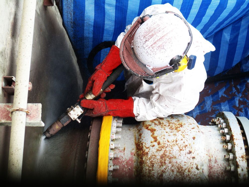 Worker Sandblasting a Rusty Pipe While Wearing Protective Gear — All Things Industrial in Mackay, QLD