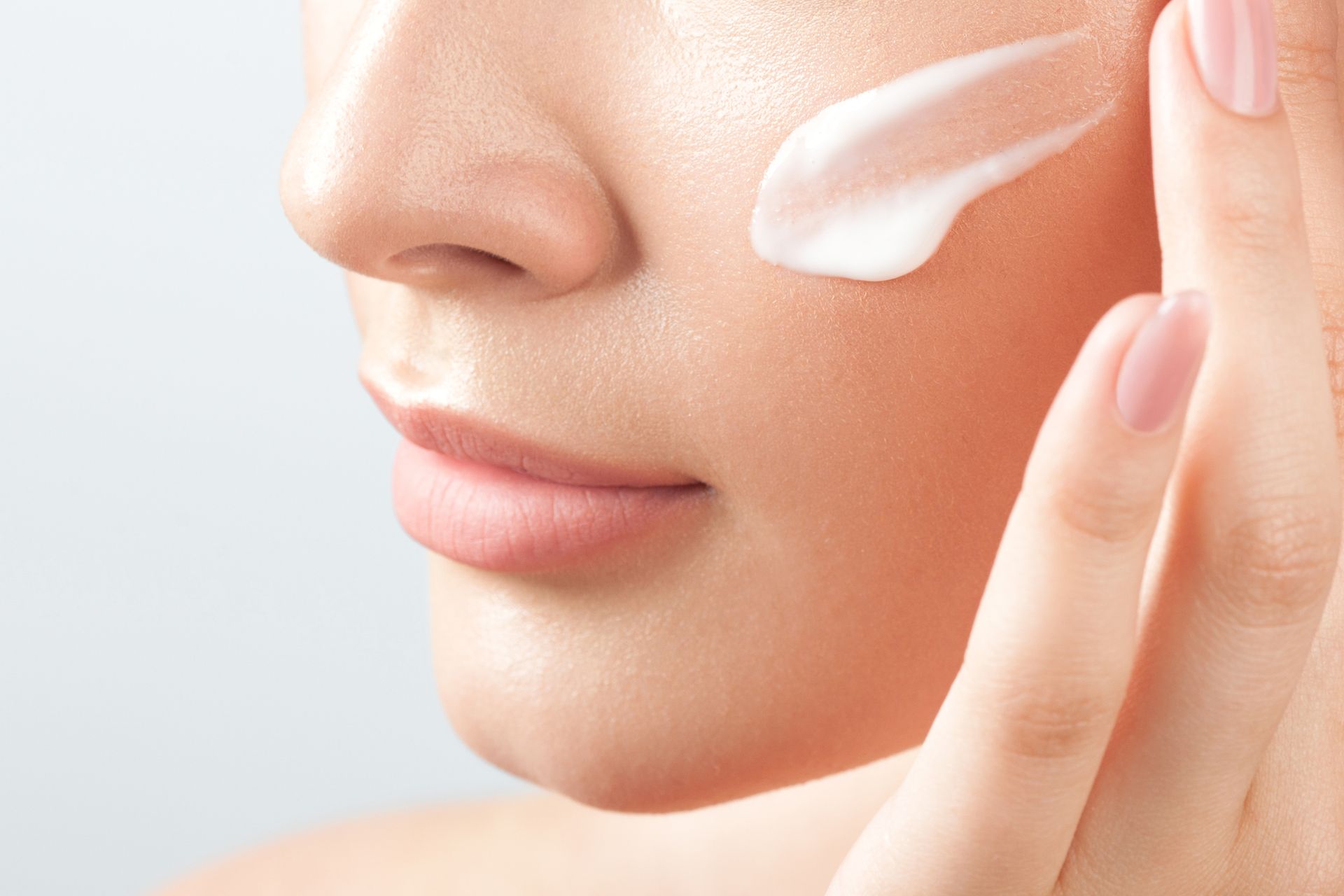 Close-up of a face applying white cream to the cheek with fingers