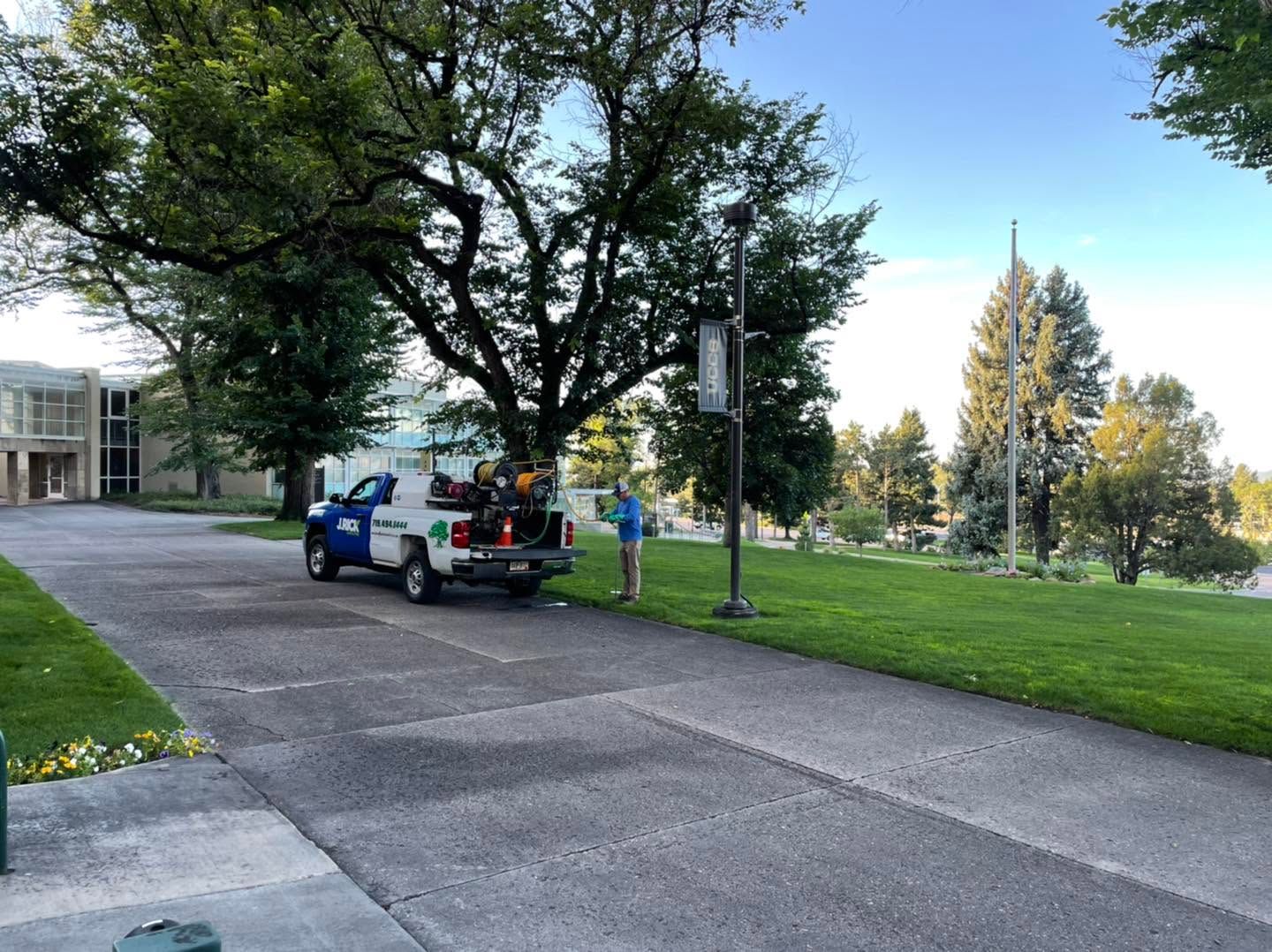 Blue car parked by a grassy campus path under large trees near a building