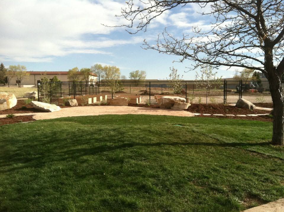 Landscaped park with green lawn, paths, benches, and a tree under a blue sky