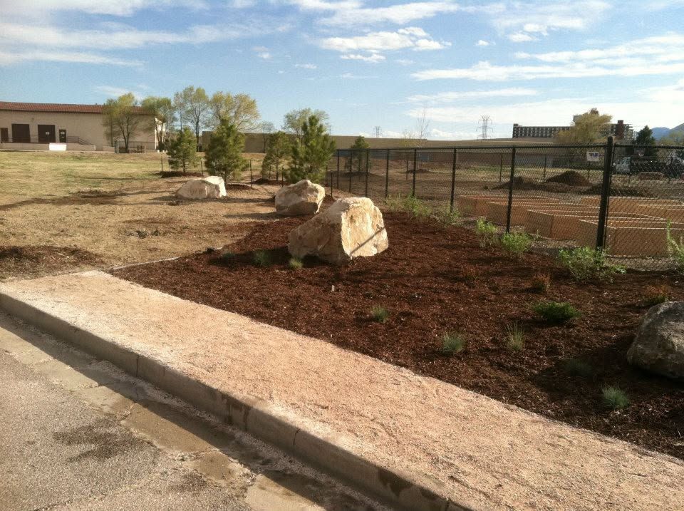 Landscaped roadside with rocks, mulch, and a chain-link fence under a clear sky