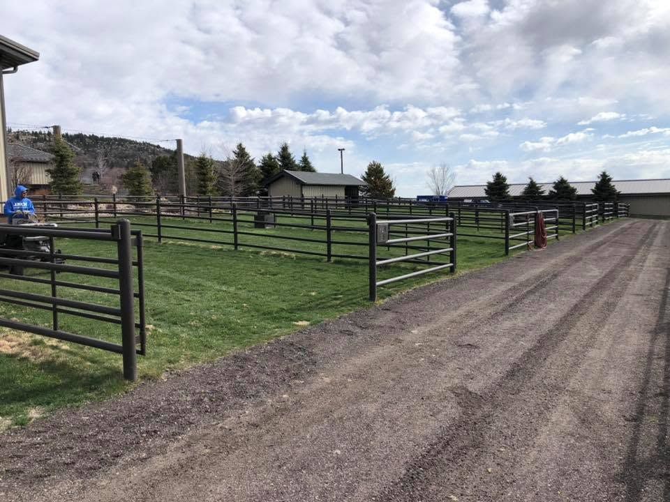 Gravel ranch road beside fenced green pasture under a cloudy sky