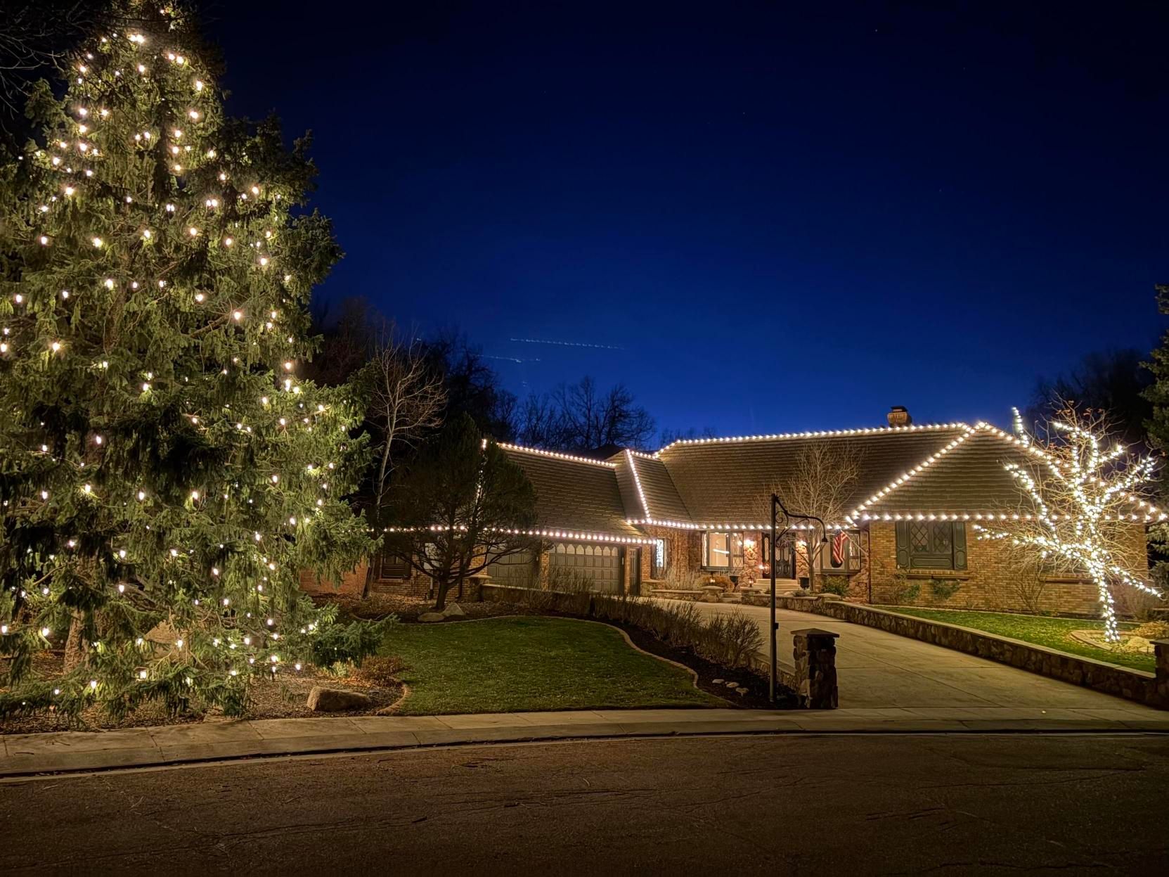A house and large Christmas tree lit with warm white lights at night under a deep blue sky