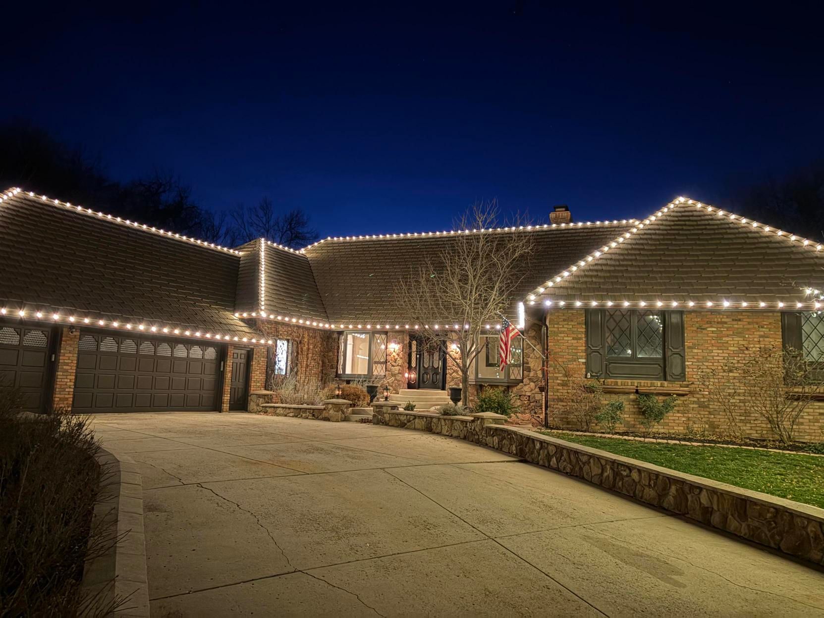 Single-story house with lit roofline at night, stone exterior, driveway, and garage
