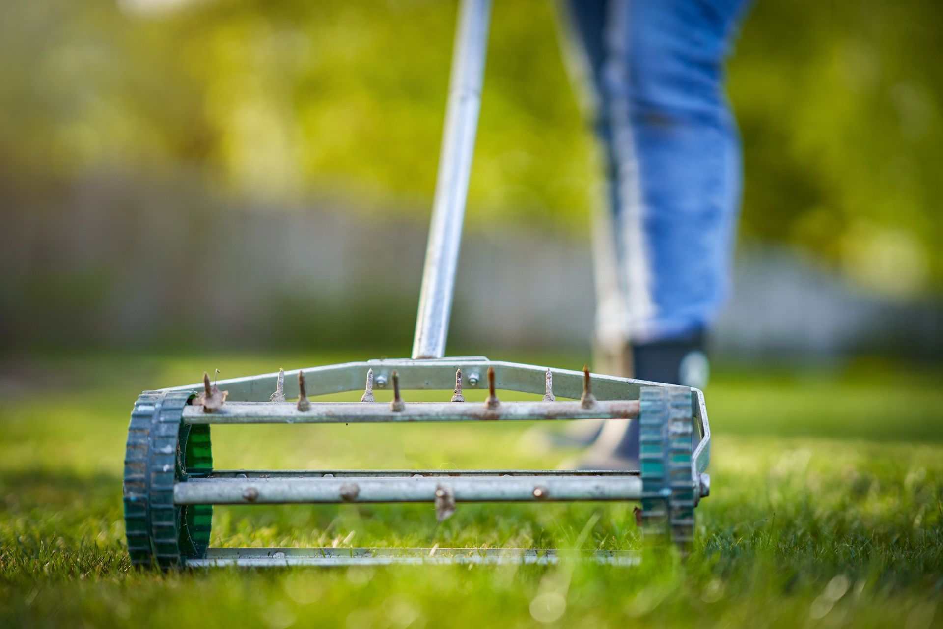 A lawn mower on green grass with a person pushing it in the background