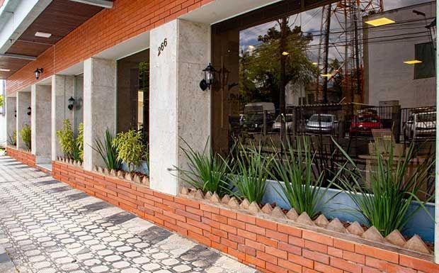 Exterior do restaurante com fachada de tijolos e vidro, floreiras e calçada.