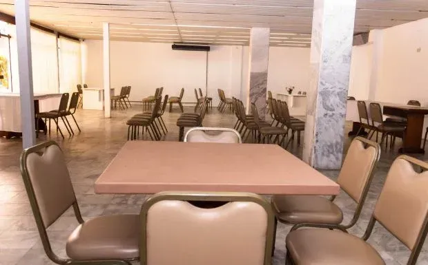 Sala de jantar bege vazia com muitas cadeiras ao redor de mesas.