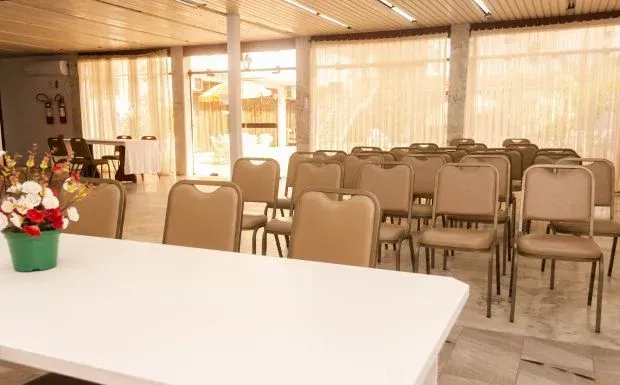 Sala de reuniões vazia com cadeiras bege e uma mesa branca. Luz proveniente das janelas.