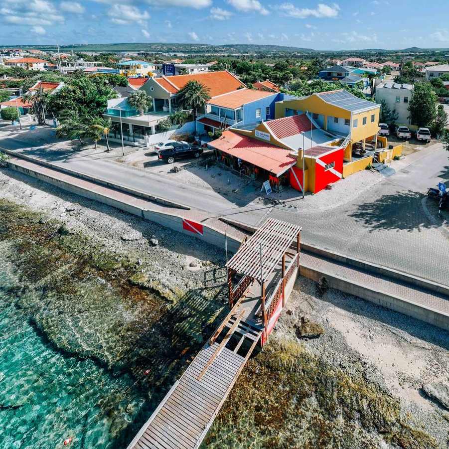 Coastal town waterfront Bonaire with colorful buildings, boardwalk, and turquoise water beside a rocky shore.