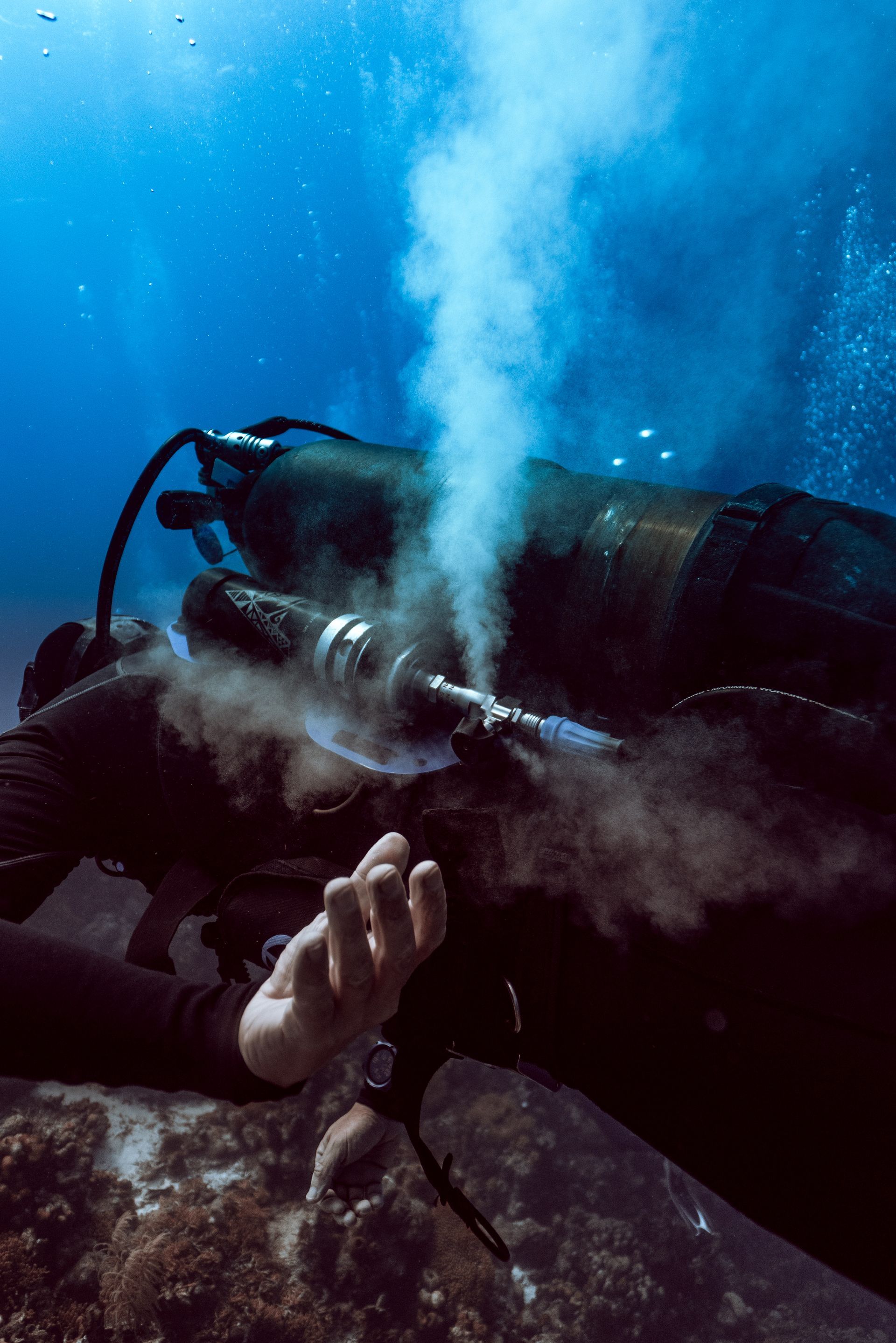 Dive Friends Scuba diver underwater releasing bubbles, with blue water and rocky seabed in view