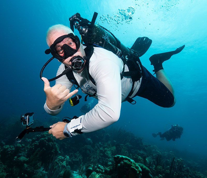 Dive Friends Scuba diver in white gear giving a thumbs-up underwater near a coral reef