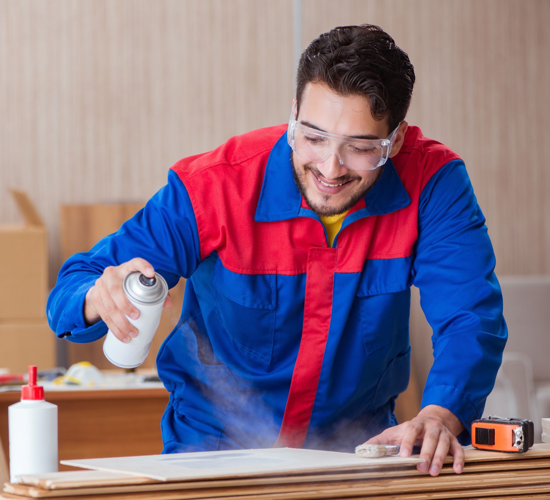 A man is spraying glue on a piece of wood.