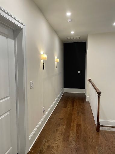A long hallway with hardwood floors and white walls leading to a staircase.