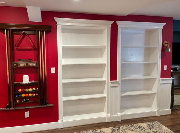A living room with red walls and white shelves and a pool table.