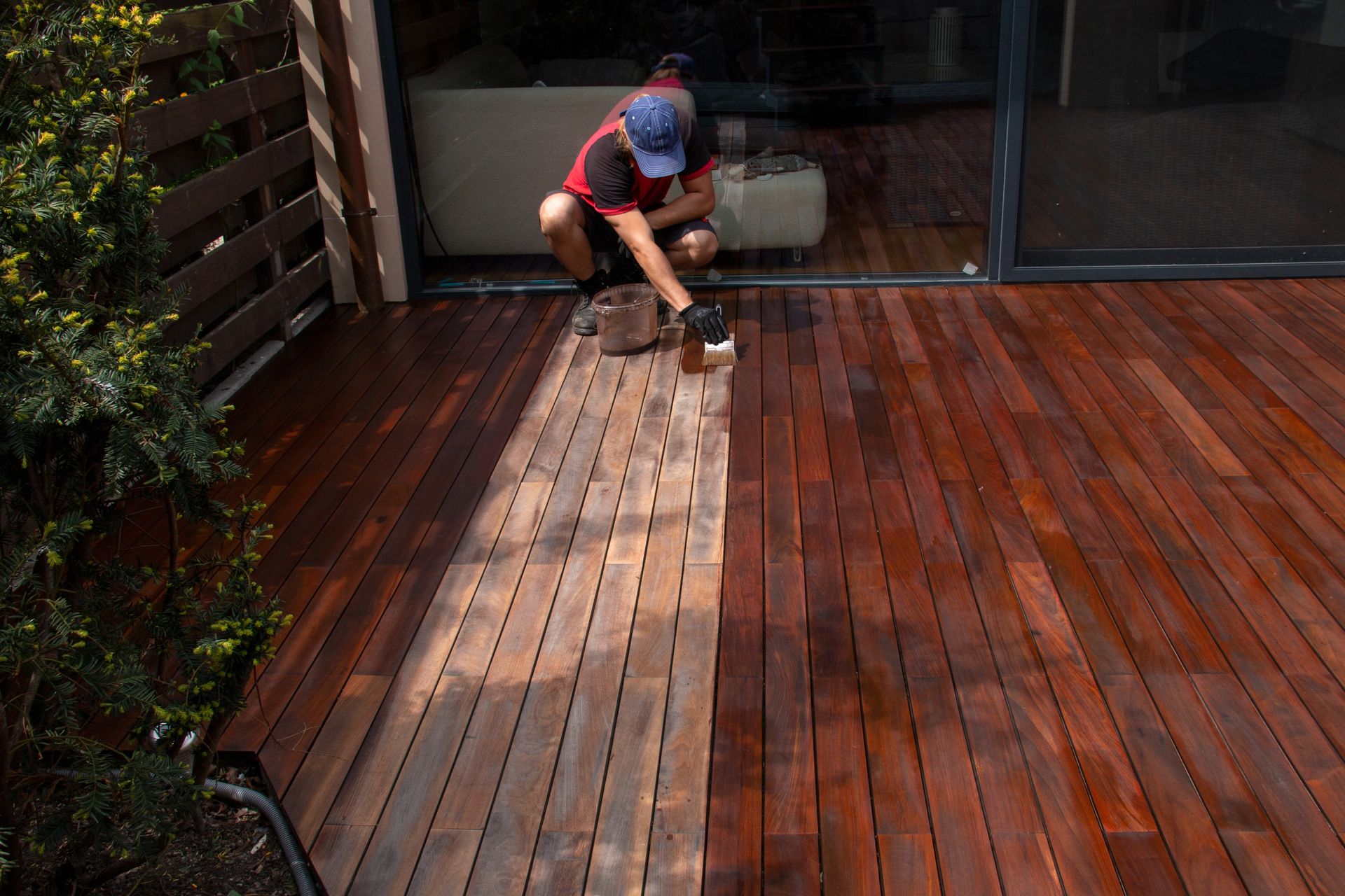 A man is painting a wooden deck with a brush.
