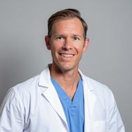 Smiling doctor in a white coat and blue scrubs against a gray background