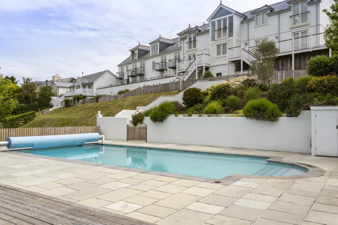 Swimming pool in front of a white building on a hill, blue pool cover and clear water.