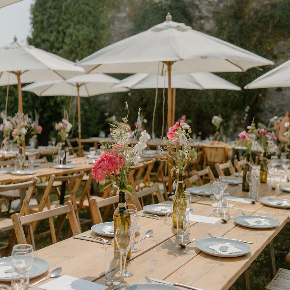 Outdoor dining tables set with floral arrangements, under white umbrellas.