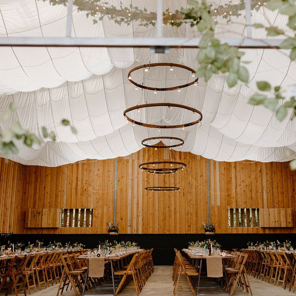 Wedding reception hall with wooden walls, long tables, and circular chandeliers.