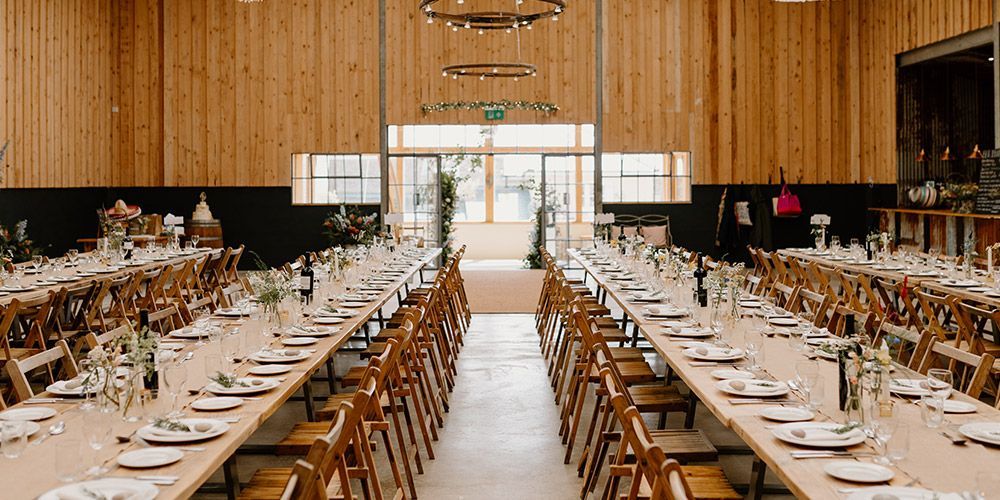 Long tables set for a banquet in a wooden hall with chairs.