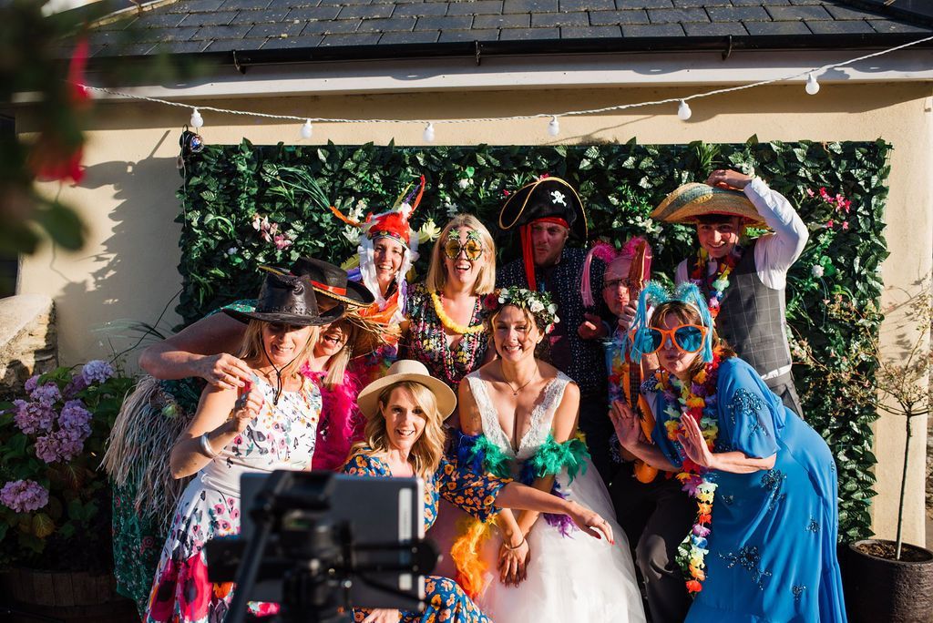 Group of people in costumes posing for photo in front of a green wall, outdoor setting, smiling, happy.