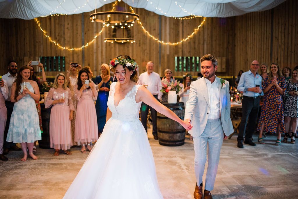 Newly married couple celebrating, holding hands, smiling, inside a barn-like venue with guests cheering.
