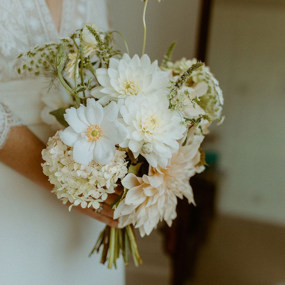 Bride holding a white and cream floral bouquet; soft light.