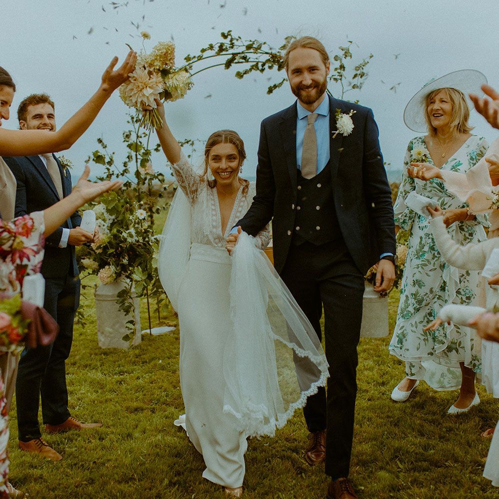 Newlyweds walk amid confetti, smiles, and flowers after their wedding ceremony.