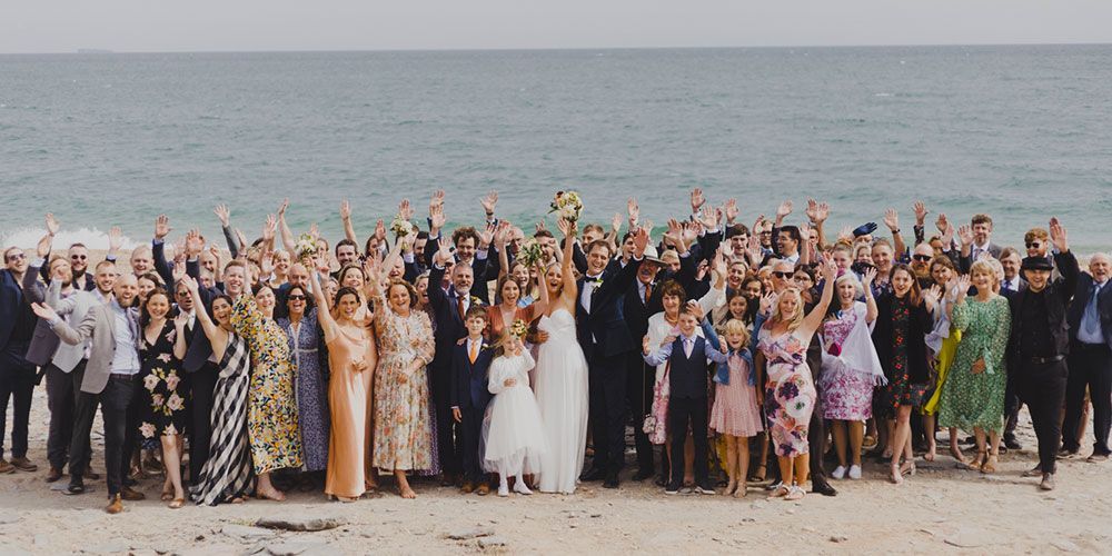 Wedding group on a beach, arms raised toward the ocean.