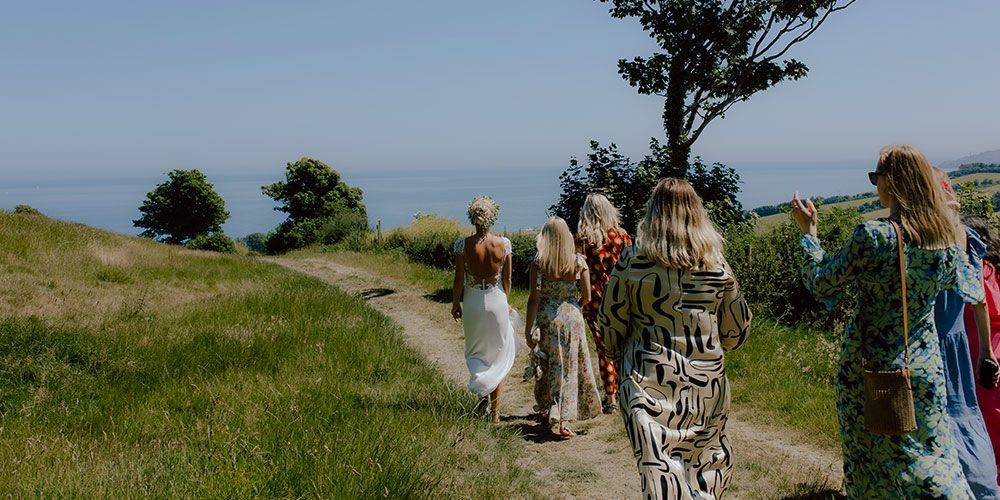 Group of people walking on a dirt path with an ocean view on a sunny day.