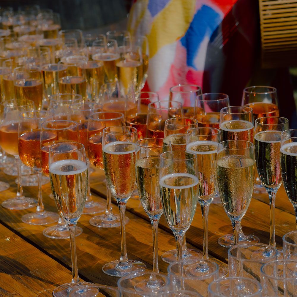Rows of champagne flutes on a wooden surface, some filled with golden and pink bubbly drinks.